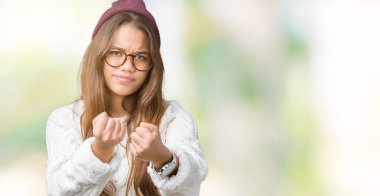 Genç güzel esmer hipster kadın gözlük ve kış şapka izole arka plan üzerinde yumruk savunma hareketi, kızgın ve üzgün yüz, sorunu korkuyor ile savaşmaya hazır
