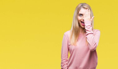 El yüz ve sürpriz duygu kendinden emin gülümseme ile tek gözüyle kapsayan izole arka plan üzerinde pembe kış kazak giyen genç güzel sarışın kadın.