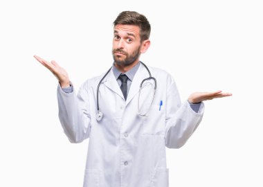 Genç yakışıklı adam izole arka plan clueless ve şaşkın bir ifadeyle kollar ve eller kaldırdı üzerine doktor. Şüphe kavramı.