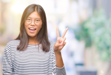 Mutlu yüz zafer işareti yaparken kameraya göz kırpıyor ile gülümseyen izole arka plan üzerinde gözlük takan Genç Asyalı kadın. İki numaralı.