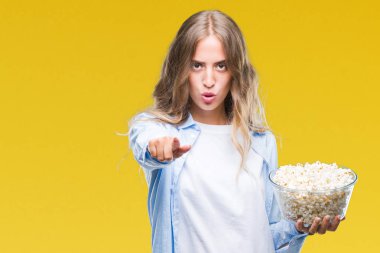 Kamera ve size parmak ile işaret arka plan üzerinde patlamış mısır yemek güzel sarışın genç kadın izole, el işareti, pozitif ve kendinden emin bir jest ön