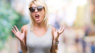 Genç güzel sarışın kadın üzerinde güneş gözlüğü takıyor arka plan deli izole ve deli bağırarak ve agresif ifade ve silah kaldırdı bağırıyor. Hayal kırıklığı kavramı.