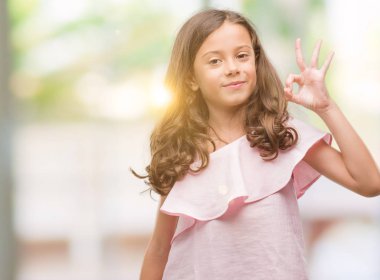 El ve parmaklar ok işaretiyle yapıyor olumlu gülümseyen pembe elbise esmer Latin kız. Başarılı ifade.