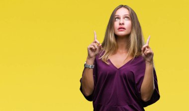 Genç güzel sarışın zarif kadın izole arka plan üzerinden hayran ve yukarıya bakıyor ve parmakları ile işaret ve silah kaldırdı şaşırttı.