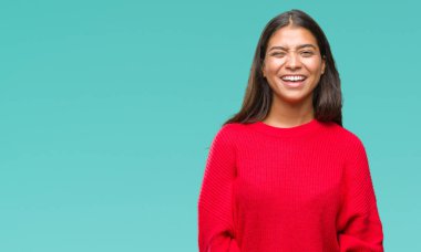 Seksi bir ifadeyle, neşeli ve mutlu yüzünü kameraya bakarak göz kırpıyor izole arka plan üzerinde kış kazak giyen genç güzel Arap kadın.