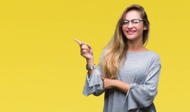 Kameraya bakarak yan el ve parmak ile işaret yüzünde kocaman bir gülümseme ile izole arka plan üzerinde gözlük takan genç güzel sarışın kadın.