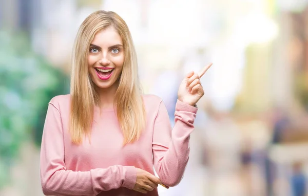 年轻美丽的金发碧眼的女人穿着粉红色的冬季毛衣在孤立的背景与一个很大的微笑在脸上 用手和手指指着一边看着镜头 — 图库照片