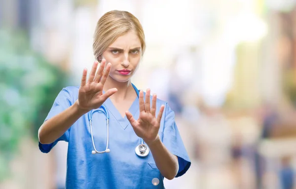 Young beautiful blonde doctor surgeon nurse woman over isolated background afraid and terrified with fear expression stop gesture with hands, shouting in shock. Panic concept.
