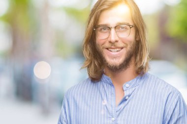 Genç yakışıklı adam uzun saçlı gözlüklü üzerinden hayran ve el ile sunulması ve parmak ile işaret ederken kameraya gülümseyen izole arka plan.