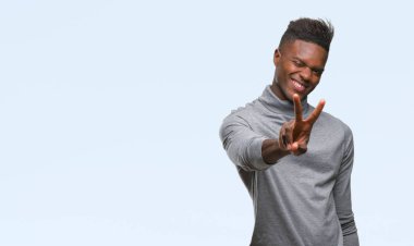 Afrikalı-Amerikalı genç zafer işareti yapıyor parmak gösterilen kamera seyir gülümseyen izole arka plan üzerinde. İki numaralı.