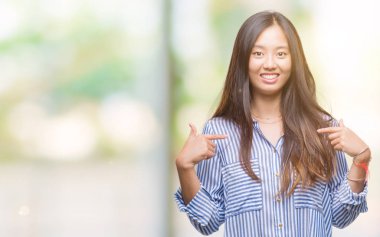 Yüzünde gülümseme ile kendinden emin görünüyorsun, kendini gururlu ve mutlu parmakları ile işaret izole arka plan üzerinde Genç Asyalı kadın.