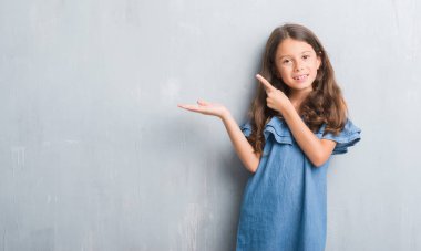 Grunge gri duvar neşeli sunulması ve kameraya bakarak avucunun ile işaret gülümseyen genç İspanyol çocuk.