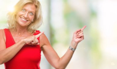 Orta yaş sarışın kadın gülümseyerek ve iki elleri ve parmakları ile tarafına işaret kamera bakarak izole arka plan üzerinde.