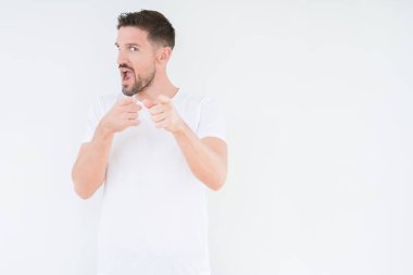 Fotoğraf makinesi ile mutlu ve komik yüz için parmakları işaret izole arka plan üzerinde rahat beyaz t-shirt giyen genç yakışıklı adam. İyi enerji ve vibes.
