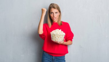 Grunge gri güzel genç kadın duvar pop corn rahatsız yeme ve boşa çıkarmak ile öfke, çılgın ve yükseltilmiş eliyle diye bağıran öfke kavramı bağırarak.