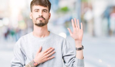 Üzerine tişört giyen genç yakışıklı adam arka plan izole göğüs ve bir sadakat sözü yemin yapma avuç, el ile küfür