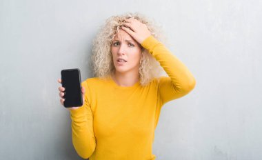 Sarışın genç kadın boş ekran başında, el ile vurguladı Smartphone gösterilen grunge gri arka plan üzerinde şok utanç ve sürpriz suratla, öfkeli ve sinirli. Korku ve hata için üzgün.