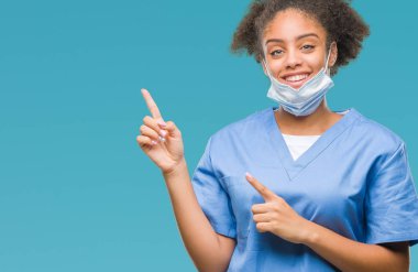 Genç afro Amerikalı doktor kadın gülümseyerek ve iki elleri ve parmakları ile tarafına işaret kamera bakarak izole arka plan.