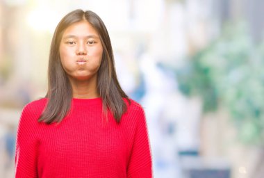 Komik surat ile yanakları şişirme izole arka plan üzerinde kış kazak giyen genç Asyalı kadın. Ağız ile hava, deli ifade şişirilmiş.