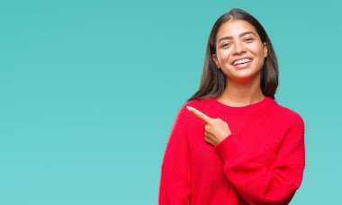 İzole arka neşeli bir gülümseme ile el ve parmak kadar kameraya bakarak yüzündeki mutlu ve doğal ifade ile yan ile işaret yüz üzerinden kış kazak giyen genç güzel Arap kadın.