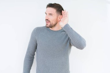 Yakışıklı genç bir işitme söylenti ya da dedikodu için dinleme kulak üzerinde el ile gülümseyen izole arka plan üzerinde rahat kazak giyiyor. Sağırlık kavramı.
