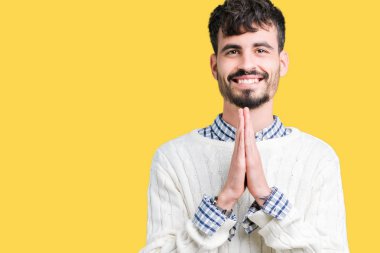 Ellerle birlikte AF emin gülümseyen için soran dua izole arka plan üzerinde kış kazak giyen genç yakışıklı adam.