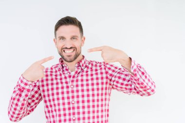 Kendinden emin gösterilen ve işaret parmakları diş ve ağız ile gülümseyen izole arka plan üzerinde gömlek giymiş yakışıklı delikanlı. Sağlık kavramı.