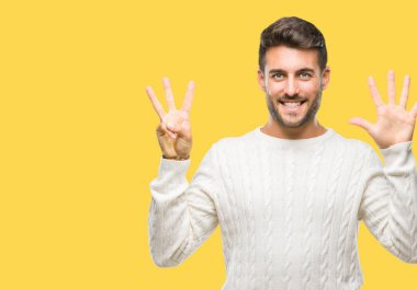 Gösterilen arka plan üzerinde kış kazak giyen genç yakışıklı adam izole ve parmakları ile işaret kendinden emin ve mutlu gülümseyerek süre 8 numaralı.