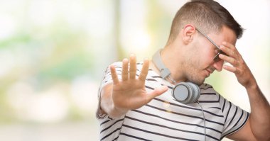 Yakışıklı genç giyen kulaklık elleriyle gözlerini kapsayan adam ve stop jest ile acı ve korku ifadesi. Utandım ve negatif kavramı.