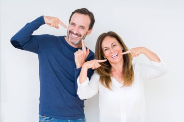 Aşk kendinden emin gösterilen ve işaret parmakları diş ve ağız ile gülümseyen izole arka plan üzerinde güzel orta yaş çift. Sağlık kavramı.