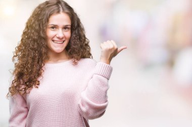 Seyir ve başparmak yanında yukarıyı mutlu yüz ile gülümseyen izole arka plan üzerinde pembe kış kazak giyen güzel esmer kıvırcık saçlı Genç kız.