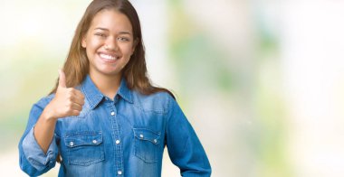 Hareketi el ile mutlu yaşasın yapıyor izole arka plan üzerinde mavi kot gömlek giyen genç güzel esmer kadın. Başarı gösteren kameraya bakarak ifade onaylama.