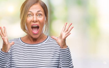 Orta yaş üst düzey İspanyol kadın deli kutluyor arka plan izole ve başarı için kaldırdı kollarını açarak hayrete ve heyecanlı çığlık gözleri açık. Kazanan kavramı