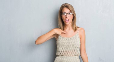 Sürpriz yüz işaret parmağı kendine gözlük grunge gri duvar üzerinde duran güzel genç kadın