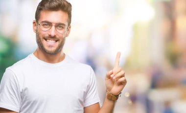 Kameraya bakarak yan el ve parmak ile işaret yüzünde kocaman bir gülümseme ile izole arka plan üzerinde gözlük takan genç yakışıklı adam.