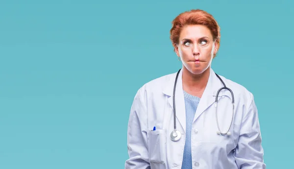 Senior caucasian doctor woman wearing medical uniform over isolated background making fish face with lips, crazy and comical gesture. Funny expression.