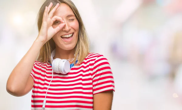 幸せそうな顔で指を通して見る目の手で のジェスチャーを行う分離の背景にヘッドフォンを着て音楽を聴く若い美しい女性 — ストック写真