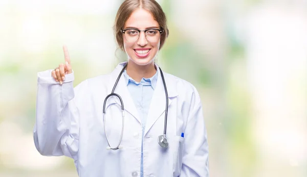 美丽的年轻金发碧眼的医生妇女穿着医疗制服在孤立的背景显示和手指第一指向 而微笑着自信和快乐 — 图库照片