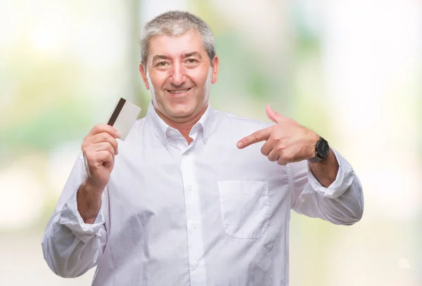 自分自身に驚き顔ポインティング指で孤立した背景の上クレジット カードを保持しているハンサムな年配の男性 — ストック写真