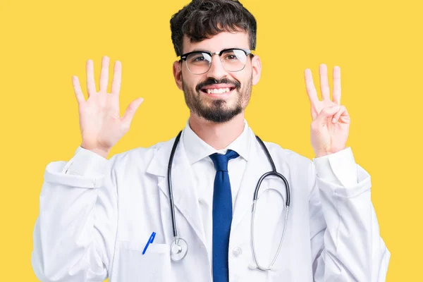 年轻的医生男子穿着医院外套在孤立的背景显示和手指指向八号 同时微笑着自信和快乐 — 图库照片