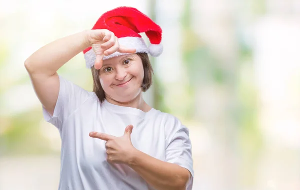 有唐氏综合症的年轻成年妇女戴着圣诞帽在与世隔绝的背景下微笑着用手和手指与快乐的脸做框架 创意与摄影理念 — 图库照片