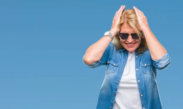 Middle age blonde woman wearing sunglasses over isolated background suffering from headache desperate and stressed because pain and migraine. Hands on head.