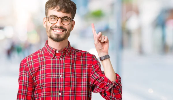 Ve kendinden emin ve mutlu gülümseyerek süre parmak numaralı yukarıyı gösteren izole arka plan üzerinde gözlük takan genç yakışıklı adam.