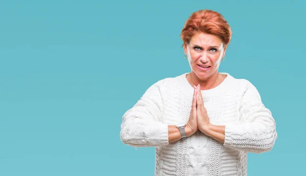 Atrractive senior caucasian redhead woman wearing winter sweater over isolated background begging and praying with hands together with hope expression on face very emotional and worried. Asking for forgiveness. Religion concept.