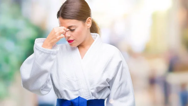 Young beautiful woman wearing karate kimono uniform over isolated background tired rubbing nose and eyes feeling fatigue and headache. Stress and frustration concept.