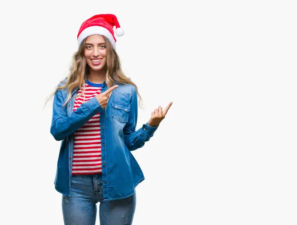分離背景笑顔で側に つの手と指で指しているカメラ目線の上クリスマス帽子身に着けている美しい若いブロンドの女性 — ストック写真