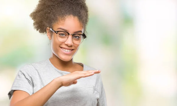 Young afro american woman wearing glasses over isolated background gesturing with hands showing big and large size sign, measure symbol. Smiling looking at the camera. Measuring concept.