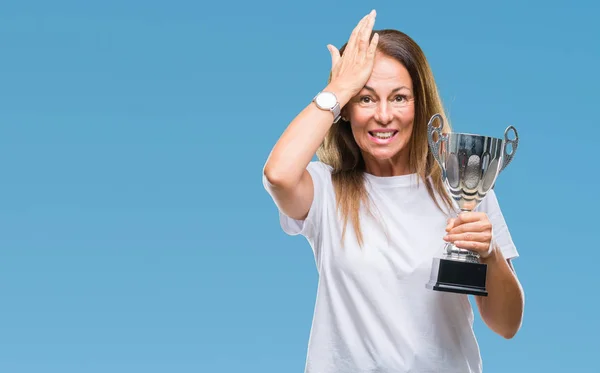 Middle age hispanic winner woman celebrating award holding trophy over isolated background stressed with hand on head, shocked with shame and surprise face, angry and frustrated. Fear and upset for mistake.