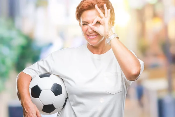 指を通して見る目に手で サインをして笑っている幸せそうな顔で孤立した背景にサッカー ボールを保持している館白人赤毛の先輩女性 — ストック写真
