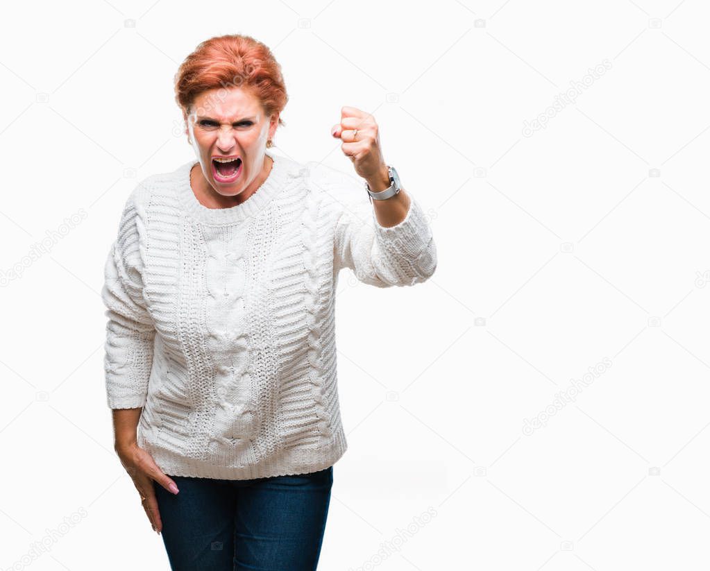 Atrractive senior caucasian redhead woman wearing winter sweater over isolated background angry and mad raising fist frustrated and furious while shouting with anger. Rage and aggressive concept.